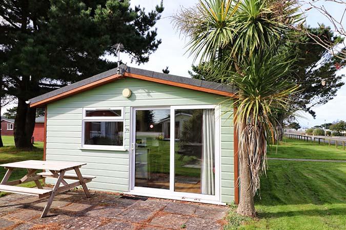 Green-painted Sun Cabin chalet exterior with picnic bench at Atlantic Bays Holiday Park
