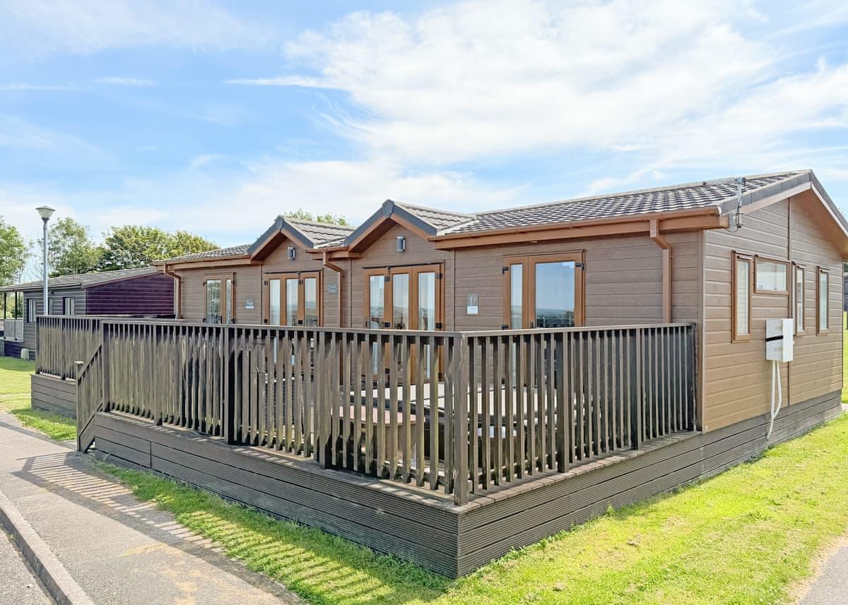 A warmly lit timber holiday lodge in the evening at Atlantic Bays Holiday Park, St Merryn