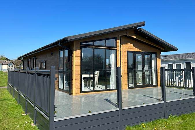 Modern oak-clad Omar Alderney lodge with glass-balustrade decking at Atlantic Bays